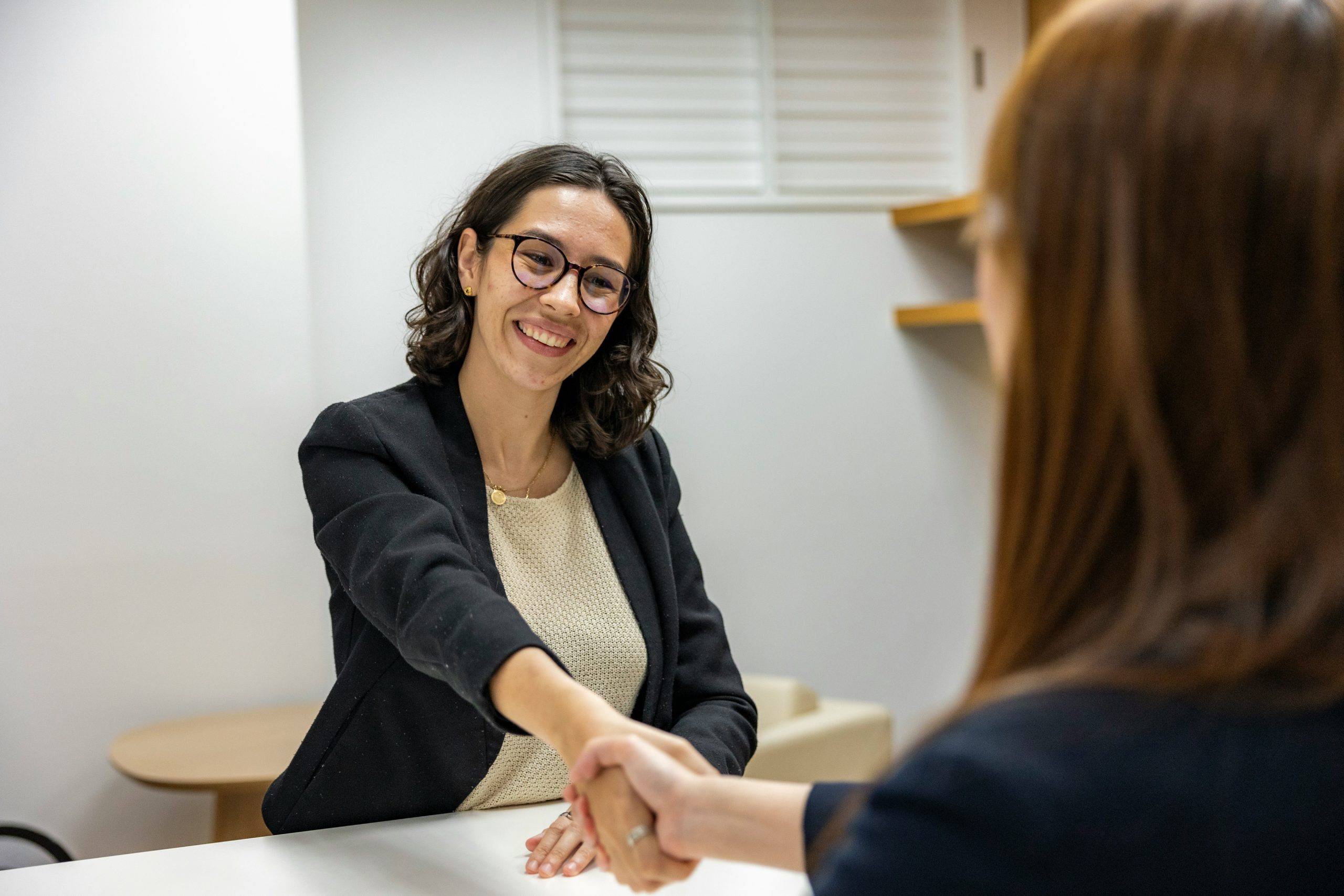 Deux femmes qui se serrent la main autour d'une table. Femme heureuse et souriante avec des lunettes.